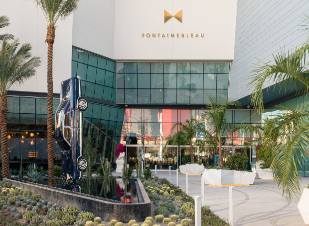 Exterior entryway with car art sculpture above water feature and plants