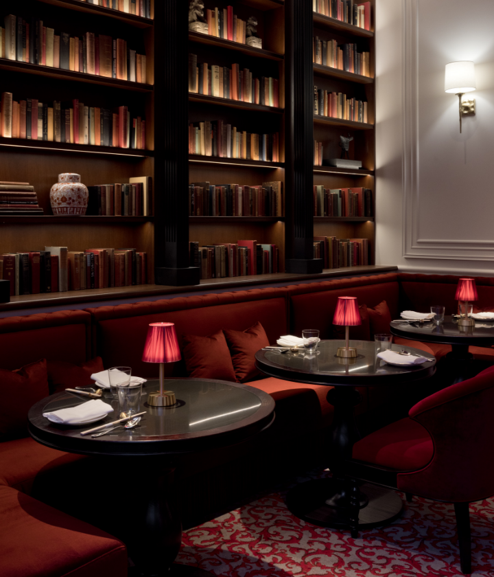 Seating area with red chairs and black tables with lamps in front of walls of books