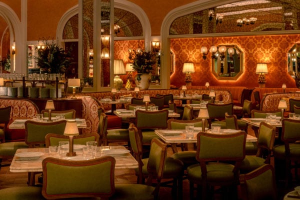 Dining space prepared with glasses, plates and lamps on tables with green chairs surrounded by booths