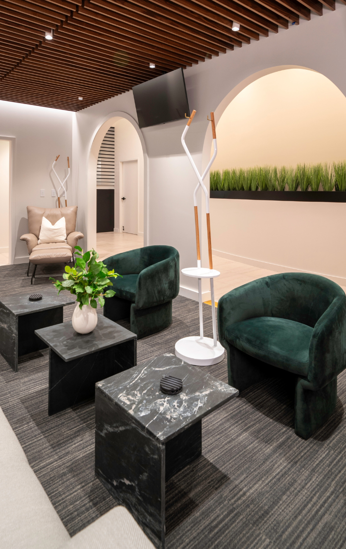 Seating area with 2 green and 1 tan chairs with tables, greenery and art sculpture