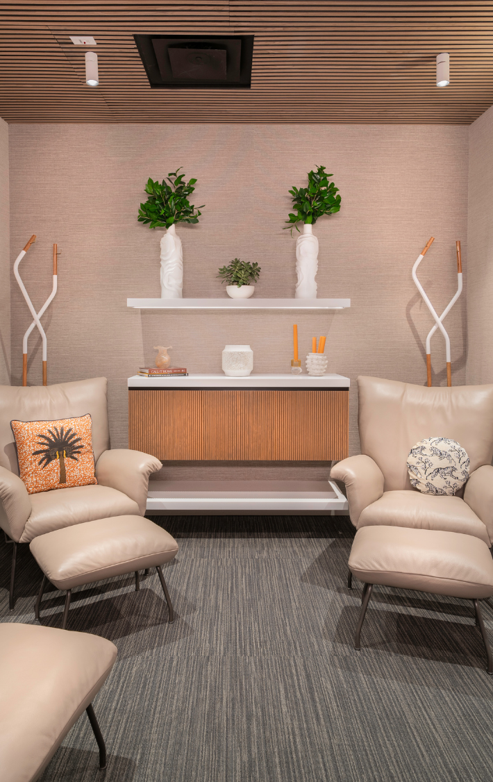 Seating area with 2 tan chairs and wall of art and plants in the background