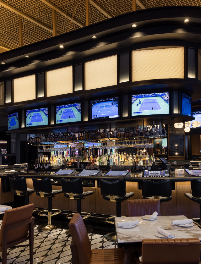 Oblong bar with televisions surrounded by stools, tables and chairs