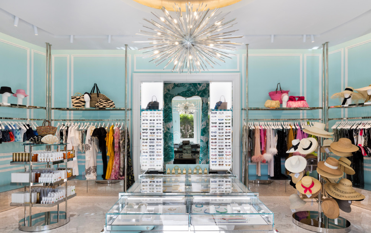 Aquamarine retail display with hat racks, jewelry cases, sunglasses and hanging clothing underneath a chandelier