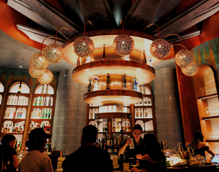 People sitting at a bar top with colorful chairs underneath metal light features