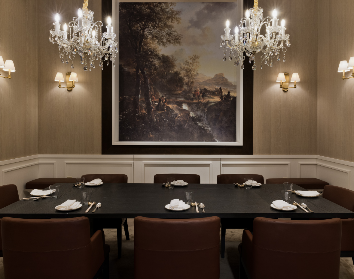 8-person black dining table with brown chairs and place settings underneath 2 chandeliers with a painting on the back wall surrounded by 4 sconces