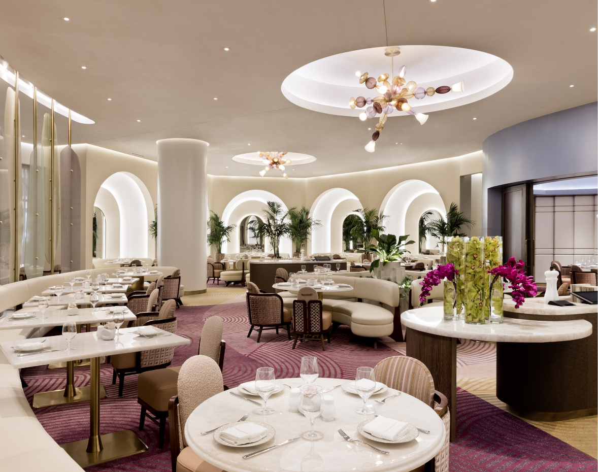 Dining space prepared with glasses, plates on tables with patterned chairs and tan couches