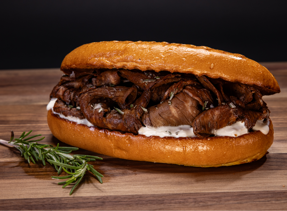 Prime beef sandwich with white sauce and rosemary garnish
