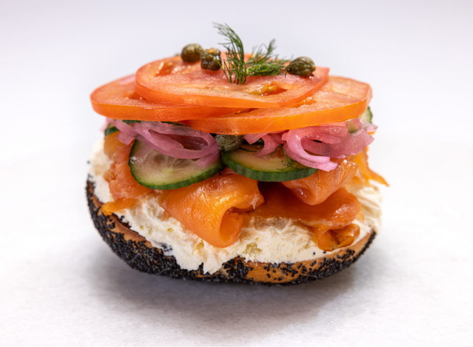 Half of bagel, covered with cream cheese, salmon, cucumber, onions, tomatoes and capers with a garnish