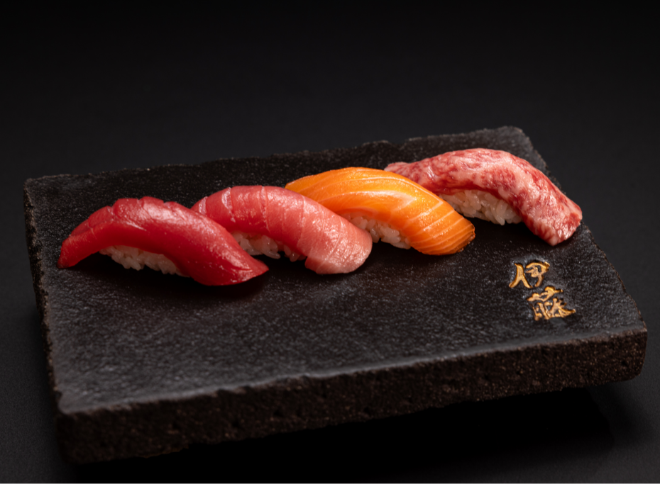 4 pieces of nigiri with gold Japanese characters embossed in a black plate