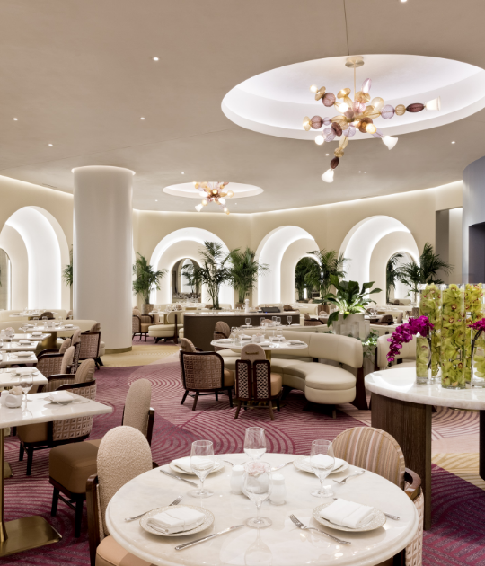 Dining space prepared with glasses, plates on tables with patterned chairs and tan couches