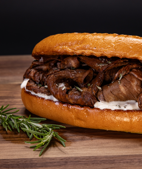 Prime beef sandwich with white sauce and rosemary garnish