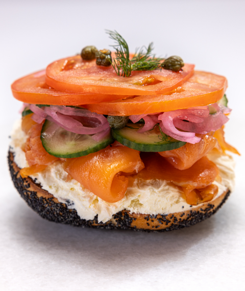 Half of bagel, covered with cream cheese, salmon, cucumber, onions, tomatoes and capers with a garnish