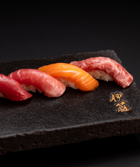 4 pieces of nigiri with gold Japanese characters embossed in a black plate