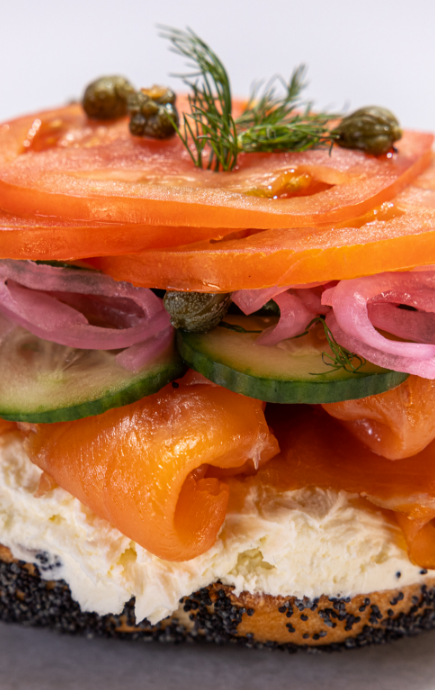 Half of bagel, covered with cream cheese, salmon, cucumber, onions, tomatoes and capers with a garnish