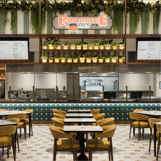 Roadside Taco sign logo hanging amongst greenery in the quick service restaurant area with seating