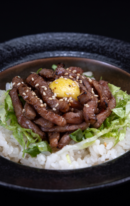 Egg, surrounded by meat over a bed of lettuce and rice in a bowl.