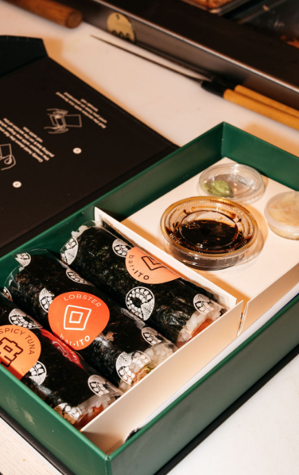 3 wrapped pieces of sushi with soy, wasabi and ginger in a green box