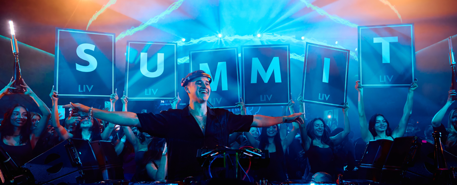 DJ with arms outspread looking out at the crowd with Summit spelled out in cards behind him