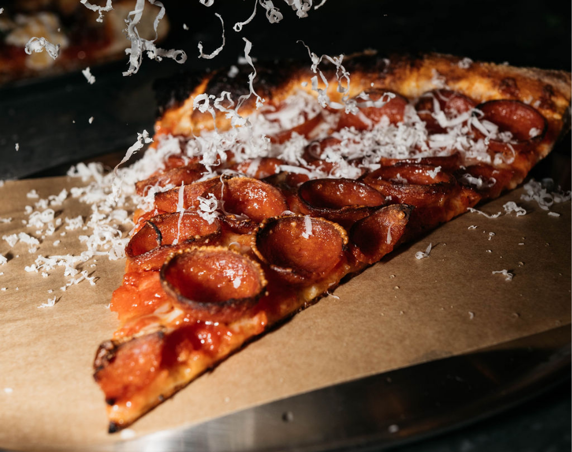 Slice of pepperoni pizza being showered with grated parmesan cheese