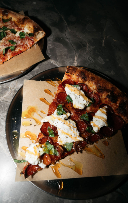 Slice of pizza topped with honey garnish, cheese and pepperoni with a second slice in the upper left corner