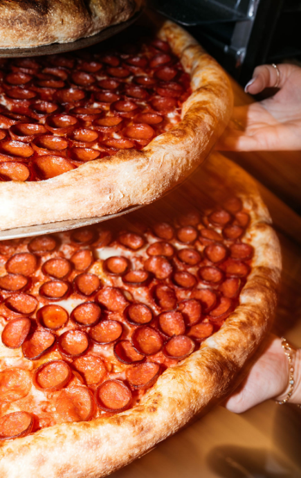 2 full pepperoni pizzas being held