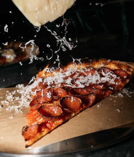 Slice of pepperoni pizza being showered with grated parmesan cheese