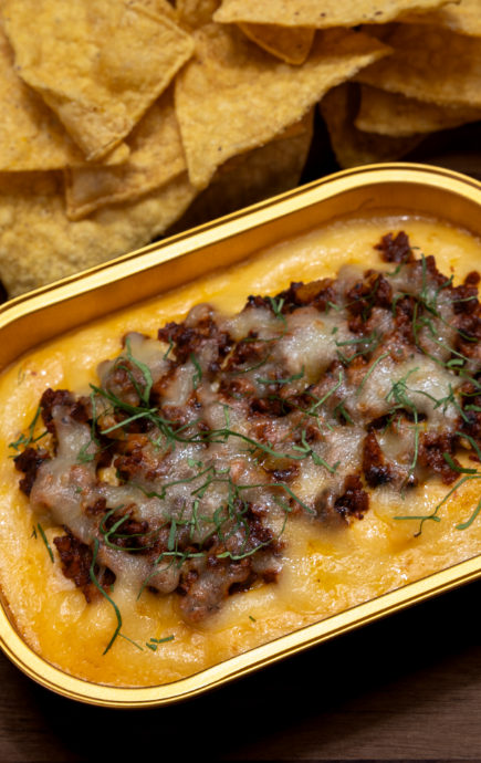 Cup of cheese with meat topping and a side of tortilla chips
