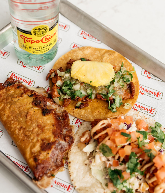 Paper lined tray with Topo-Chico mineral water and 2 open tacos and a hard taco