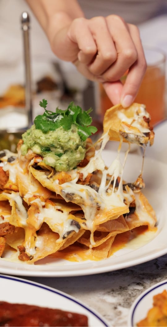 Hand pulling a nacho away from a pile of nachos with cheese stretching between them