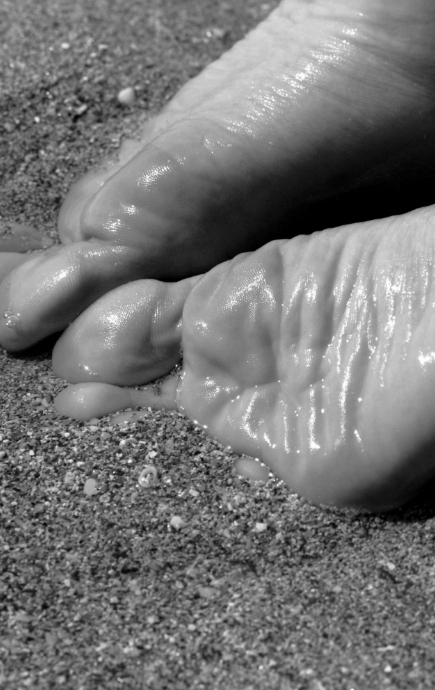 Pair of feet partially buried in sand, with soles exposed