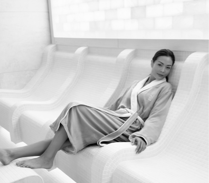 Woman in a robe sitting on a white tile chair with legs elevated