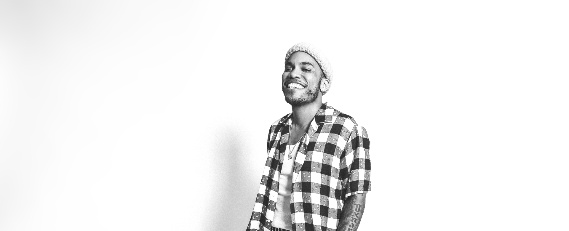 Man in plaid shirt and hat, smiling.