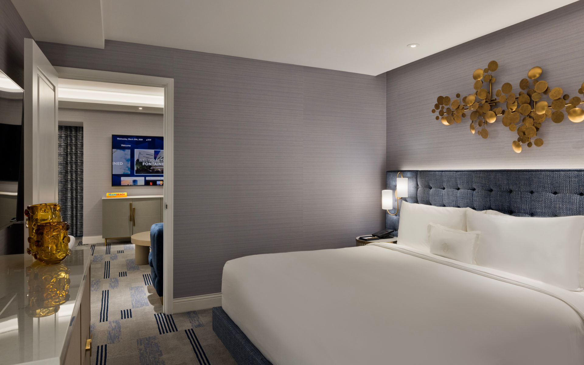 Hotel room example with bed, couch, table and art.