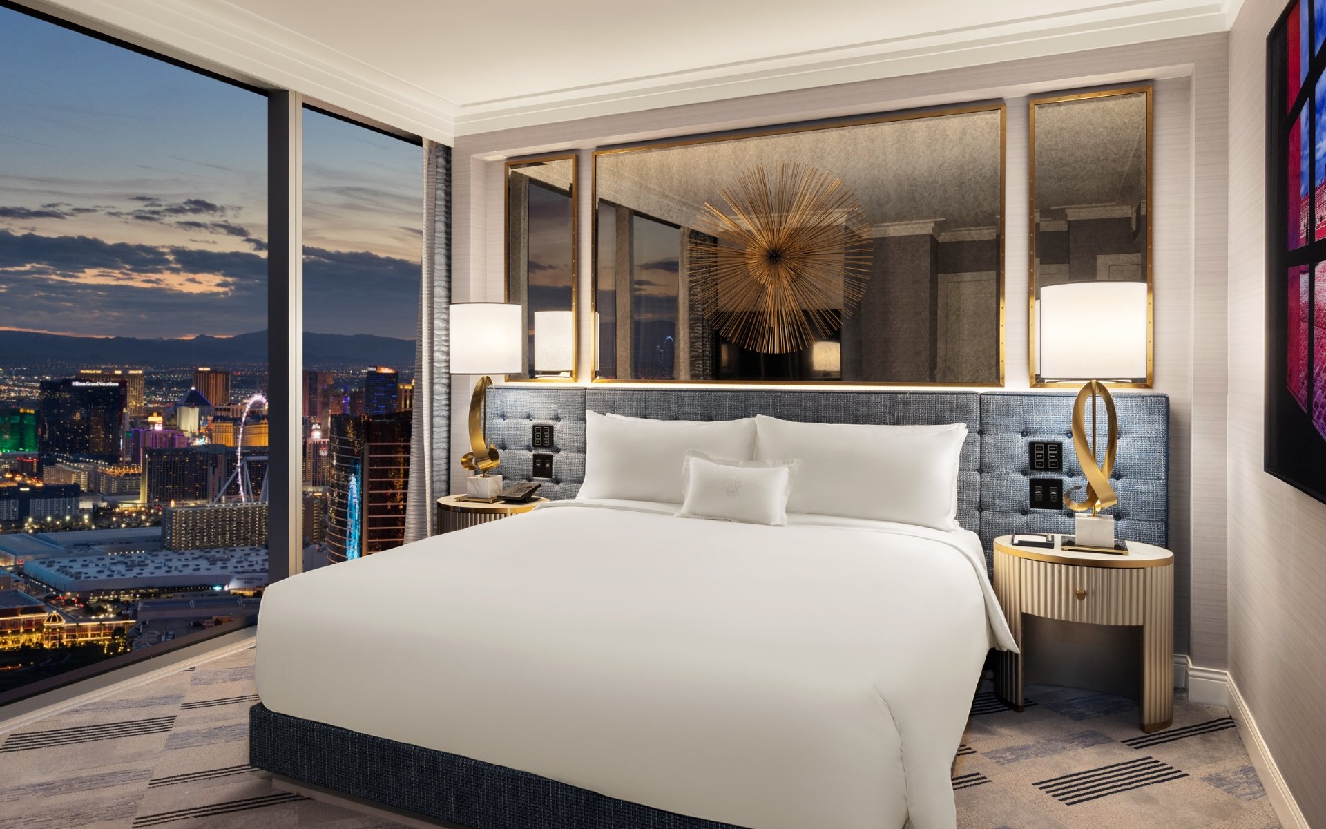 Bed framed by 2 nightstands with lamps underneath gold art piece