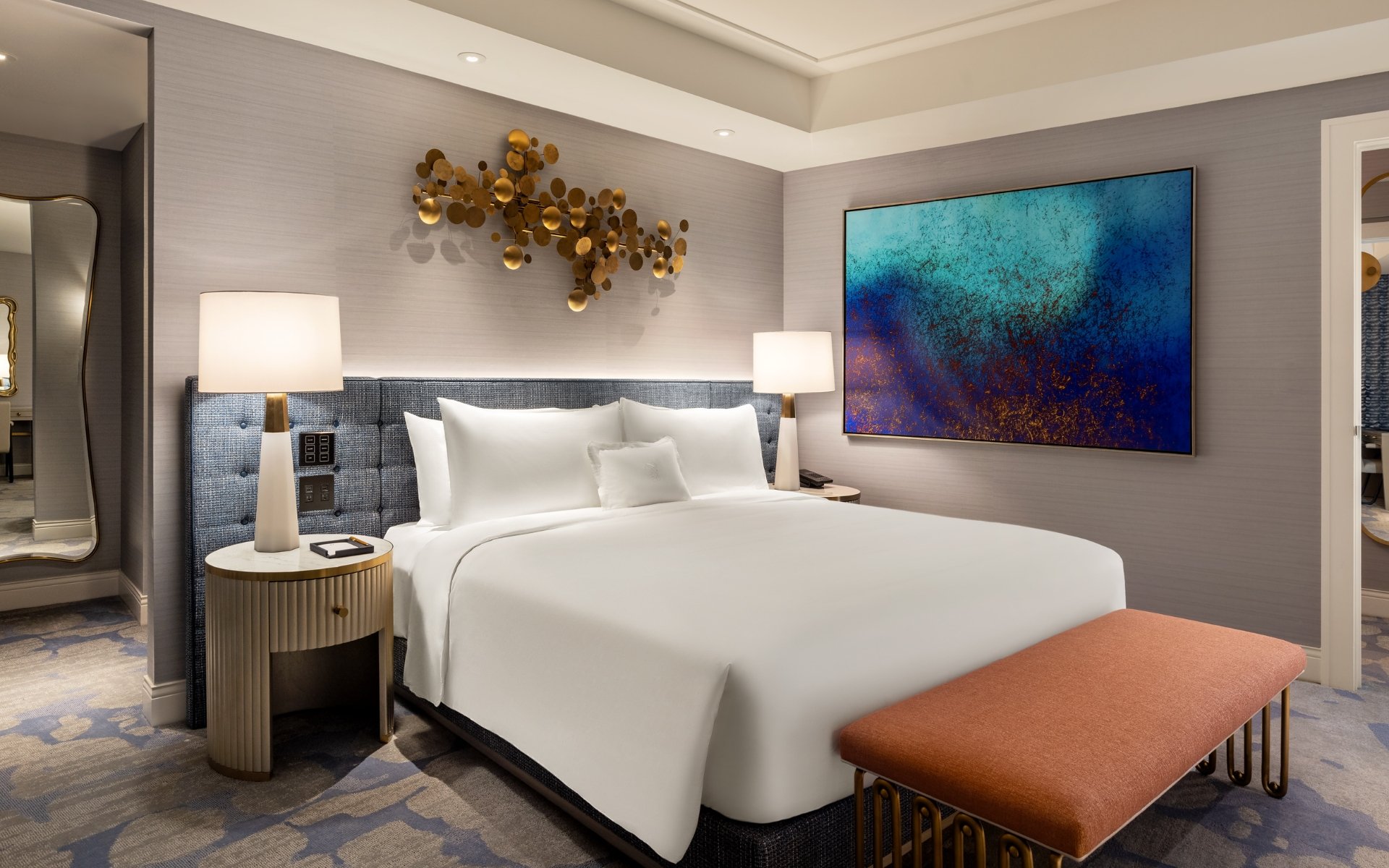 Hotel room example with bed, couch, table and art.