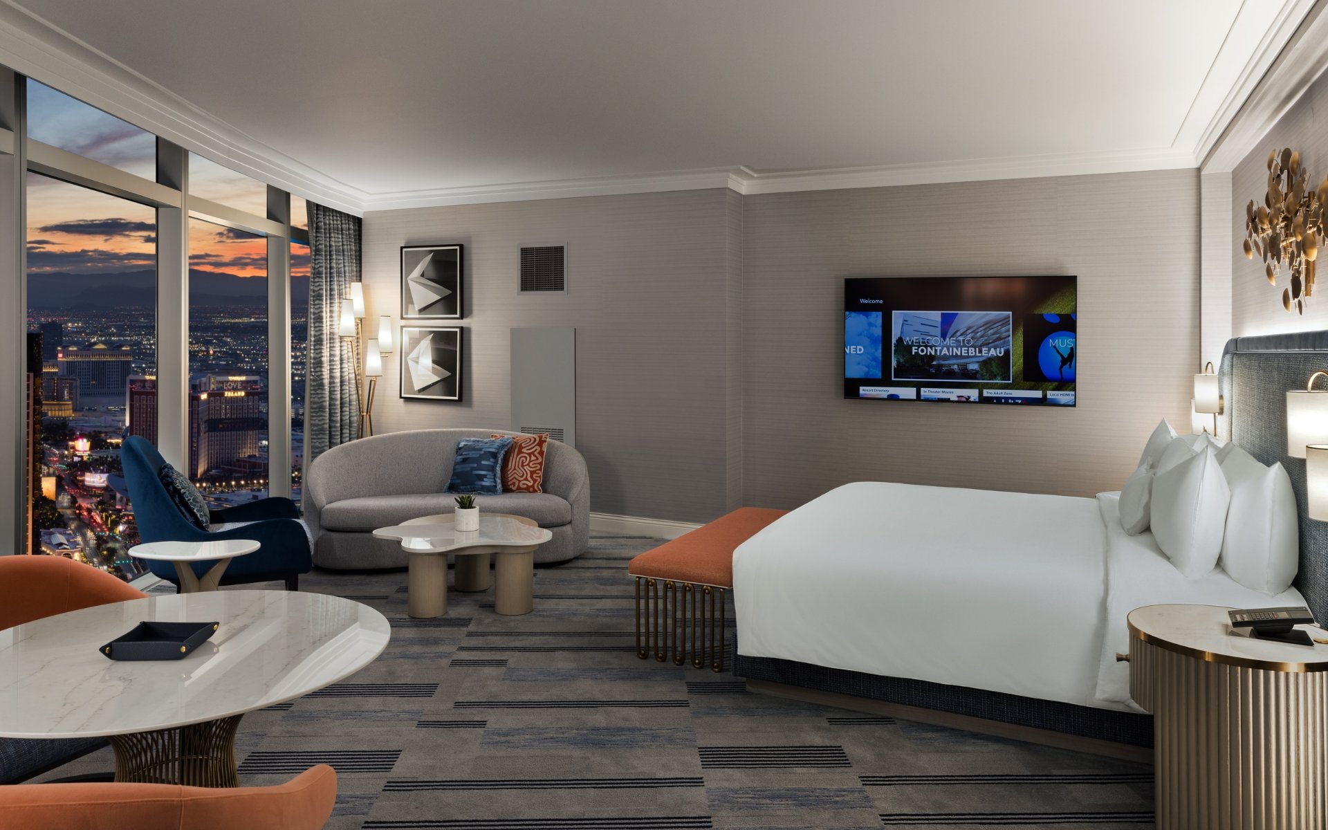 Bed framed by 2 nightstands with lamps underneath gold art piece and seating area