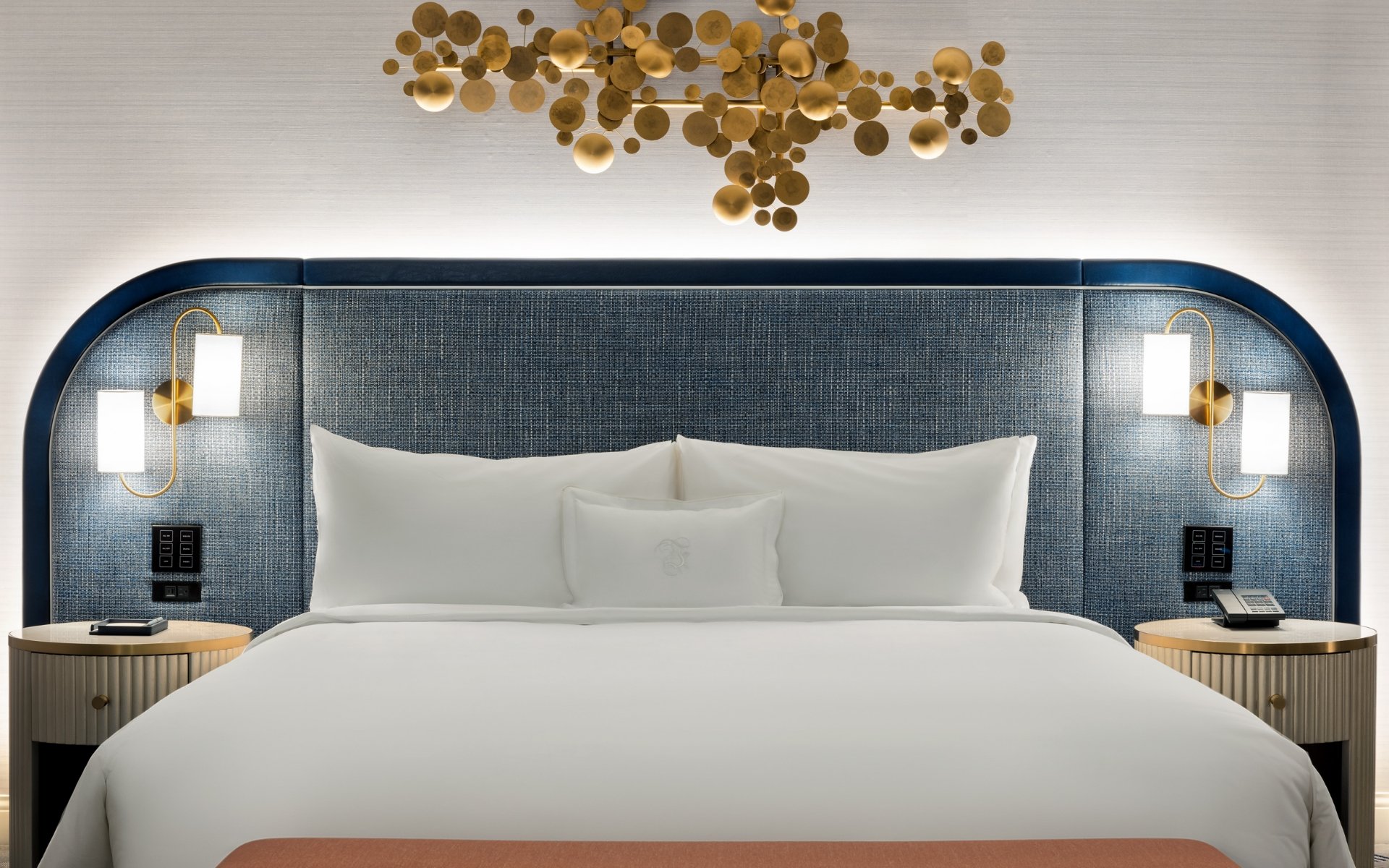 Bed framed by 2 nightstands with lamps underneath gold art piece