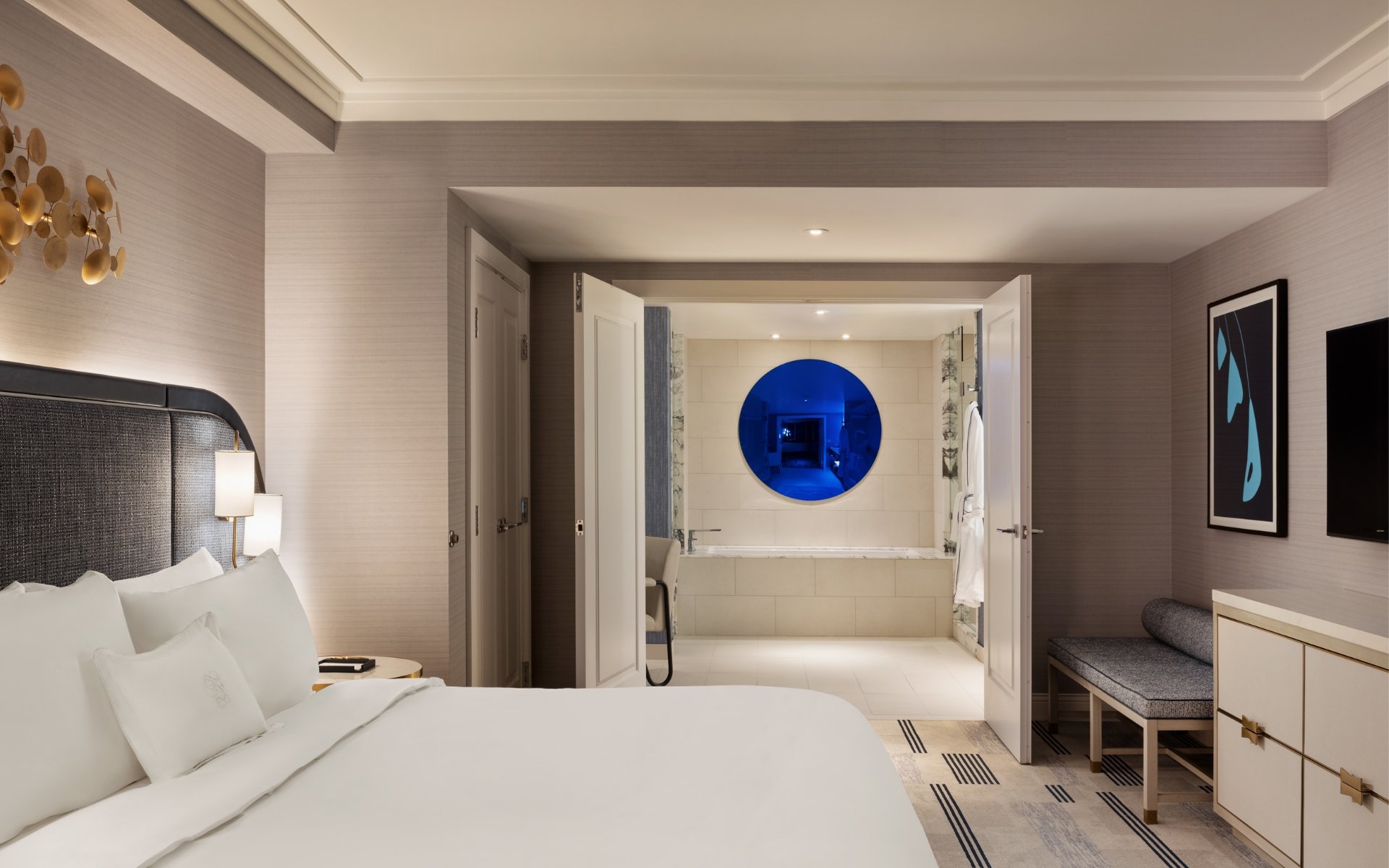 Hotel room example with bed, couch, table and art.