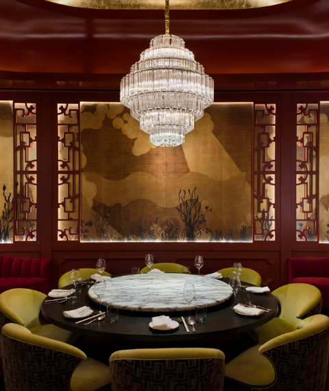 Restaurant dining space with green chairs, red walls under a chandelier.