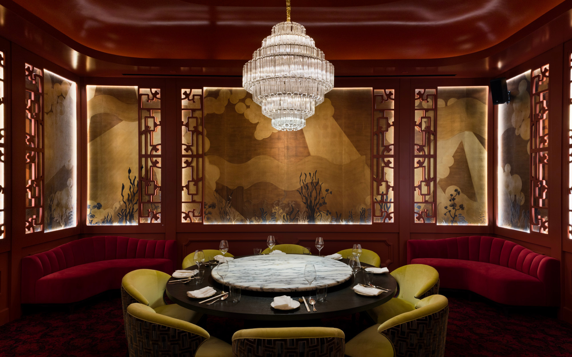 Restaurant dining space with green chairs, red walls under a chandelier.