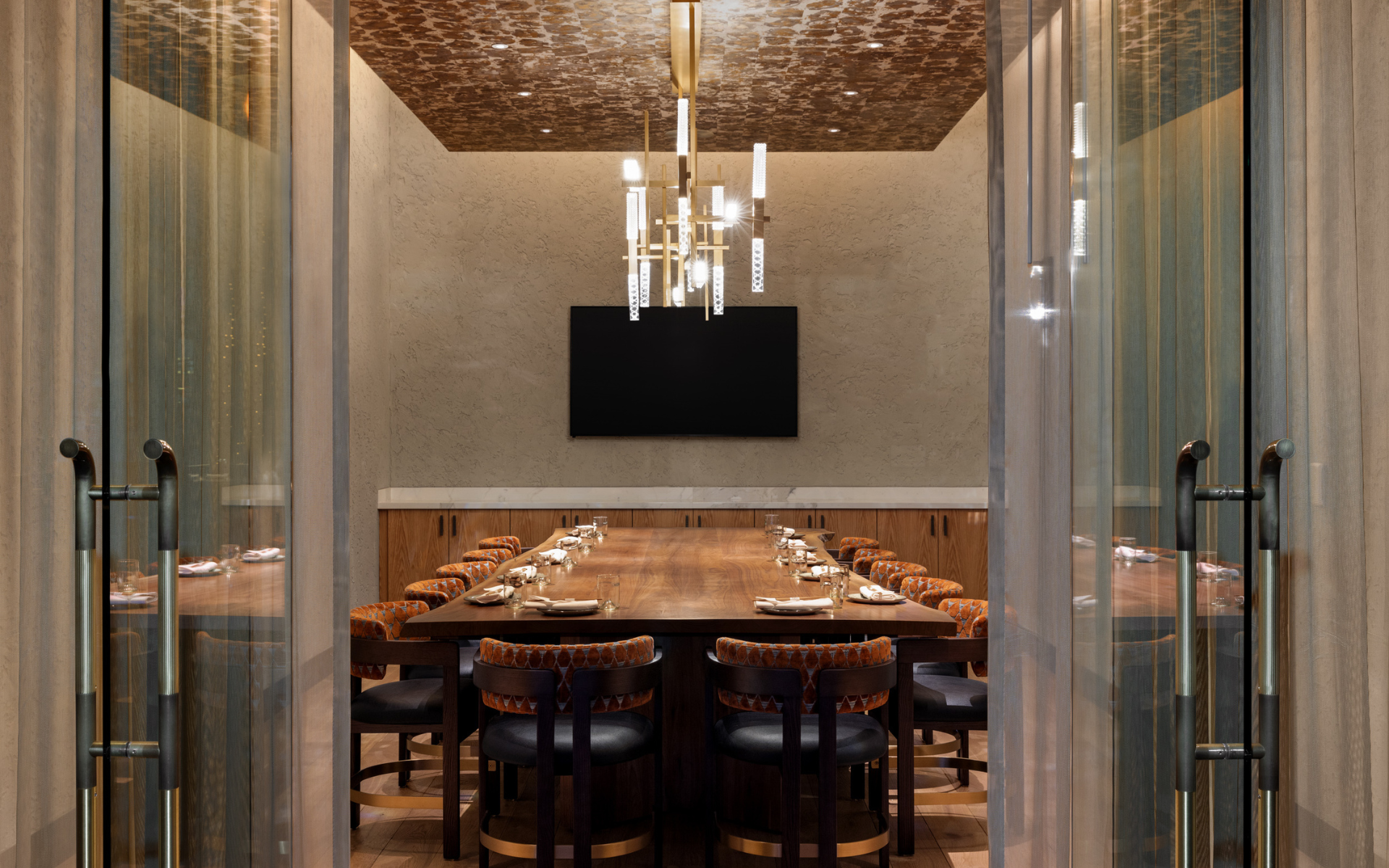 Restaurant private dining space with brown and black chairs with a wood table under a light fixture with a beige wall