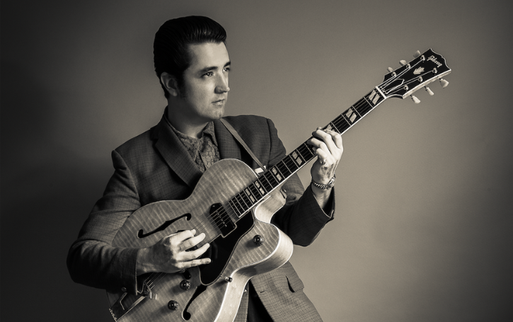 Eddie Clendening holding a guitar wearing a suit in a grey and white tonal setting