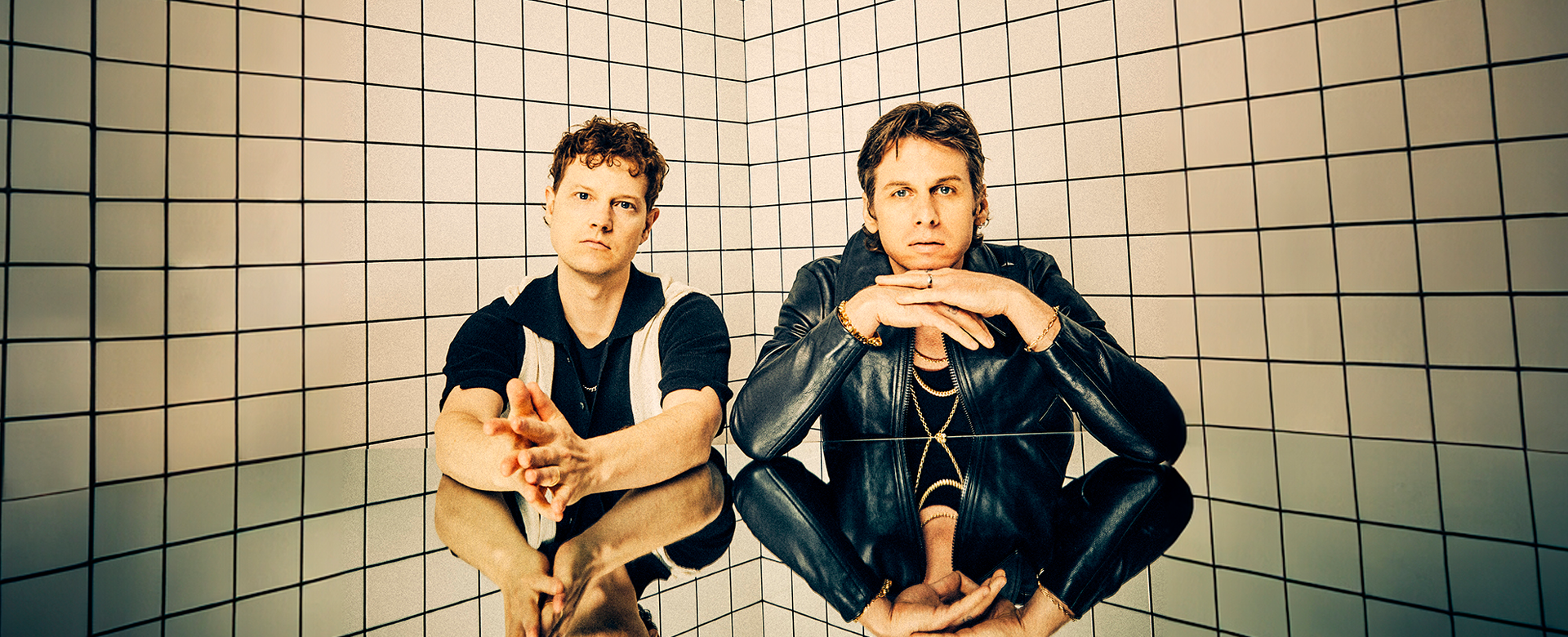 Foster the people band members sitting near a reflective surface with a textured background