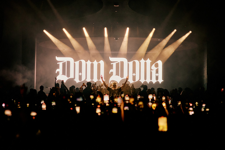 Crowded nightclub setting with Dom Dolla logo in white with cell phones lit up