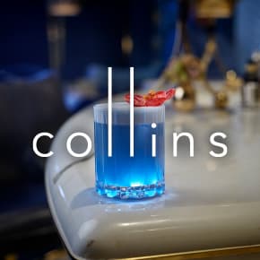 Collins logo over a blue cocktail on a white surface.