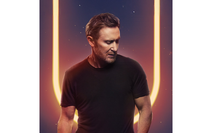 David Guetta against a dark background with yellow light.