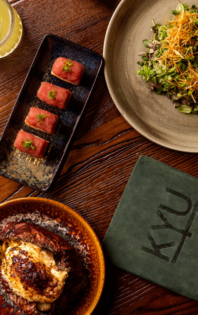 Plates of salad, chicken and sushi with KYU menu on a wooden table.