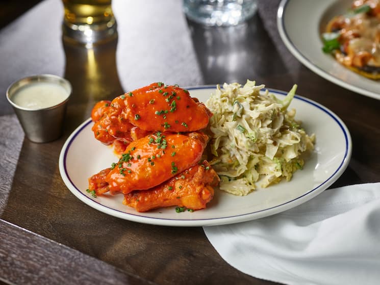 Chicken wings and coleslaw on a white plate on a brown tabletop