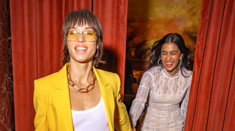 2 women holding hands walking though curtains.