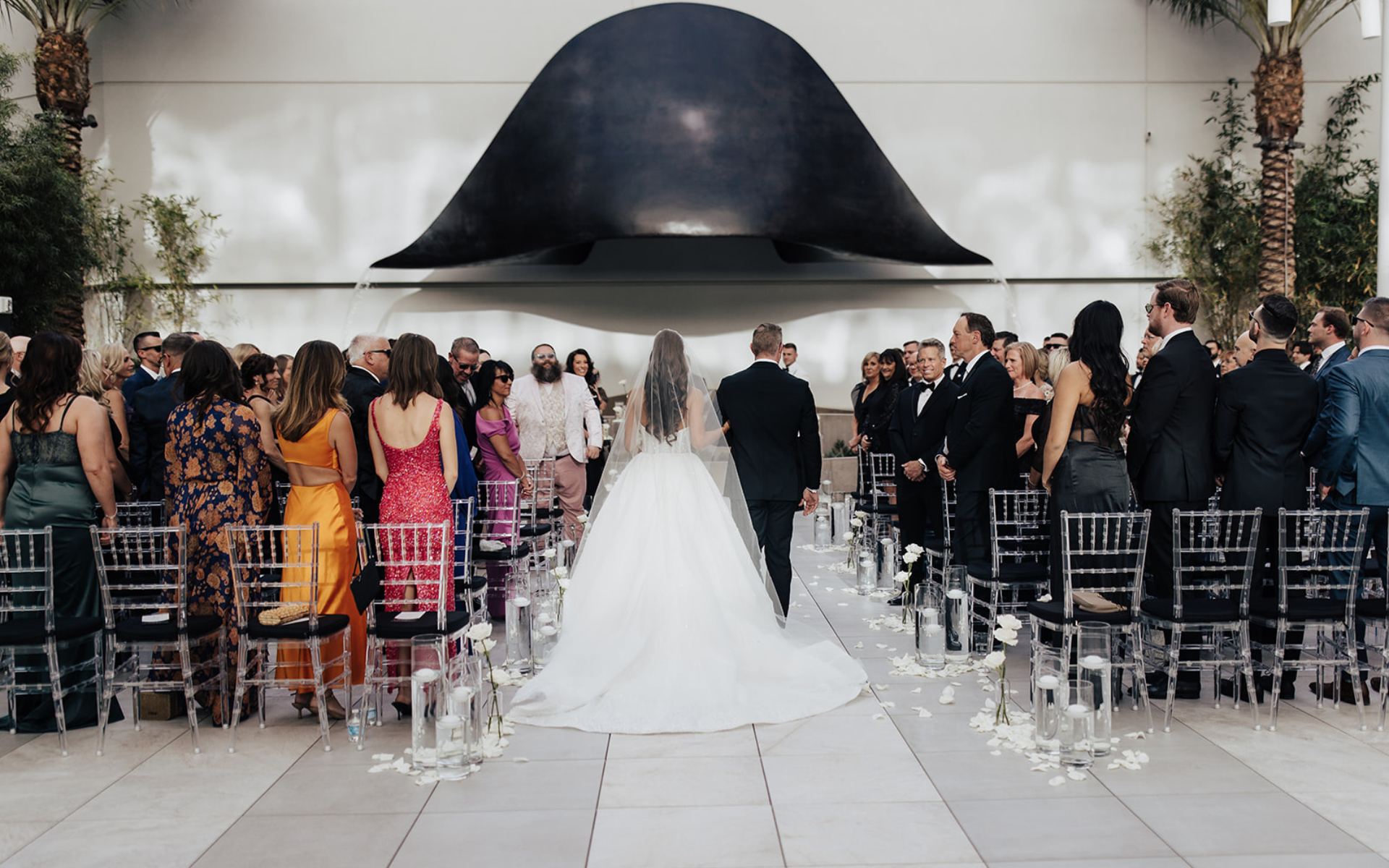 Couple walking down the aisle towards a hat statue with crowd standing watching